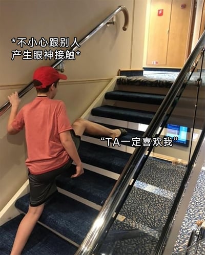 这是一张带文字加注的真人照片梗图，图中一名穿着红色短袖、黑色短裤、戴着红色帽子的男孩，在上楼梯时摆出怪异姿势：一只手抓着左侧楼梯扶手，一条腿抬起跨在楼梯台阶上。图中添加了两处文字，上方标注场景“*不小心跟别人产生眼神接触*”，下方标注男孩的内心活动““TA一定喜欢我””，用夸张的肢体动作和不符合常理的内心脑补，调侃了部分人在社交中与他人偶然对视后，产生过度自恋式脑补的搞笑心理，十分贴合日常社交中的趣味心态。