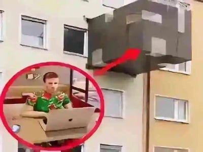 这是一张利用视觉错位制作的搞笑P图，图中楼房外突出的深色阳台部分，和下方红圈里坐在沙发前使用笔记本电脑的人物场景巧妙重合，视觉上营造出这个人悬空坐在楼房阳台外使用电脑的荒诞效果，没有双关、谐音梗等内容。
