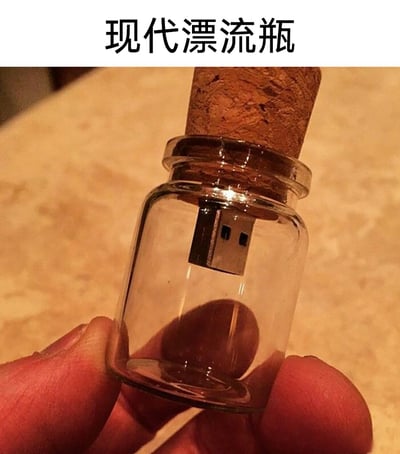 这张图片展示了一款名为“现代漂流瓶”的创意数码产品，将传统漂流瓶的外观与现代的U盘结合，把U盘的接口部分安置在带软木塞的小型玻璃瓶内，一只手用手指捏住这个玻璃瓶，形象地将存储数据的U盘类比为传递信息的传统漂流瓶，赋予了数码产品浪漫的传统意象，是兼具实用性与趣味性的创意设计。
