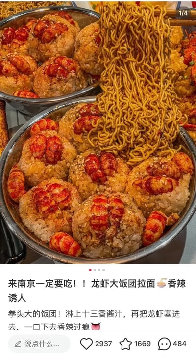 这是一张竖屏的美食实拍图文内容，展示了南京特色的小龙虾饭团拌面。画面中两大盆拳头大小的饭团十分吸睛，每个饭团都嵌入了多颗色泽红亮的小龙虾尾，表面撒有芝麻并淋上了浓郁的十三香酱汁；前景的盆中还搭配了裹满酱汁的拌面，面条被筷子夹起，油润的质感看起来香辣诱人。下方配文介绍这是南京必吃的美食，描述饭团的制作方式是淋上十三香酱汁再塞进龙虾，一口下去香辣过瘾，整体内容旨在推荐当地特色美食，无任何双关、谐音梗或暗示类内容。