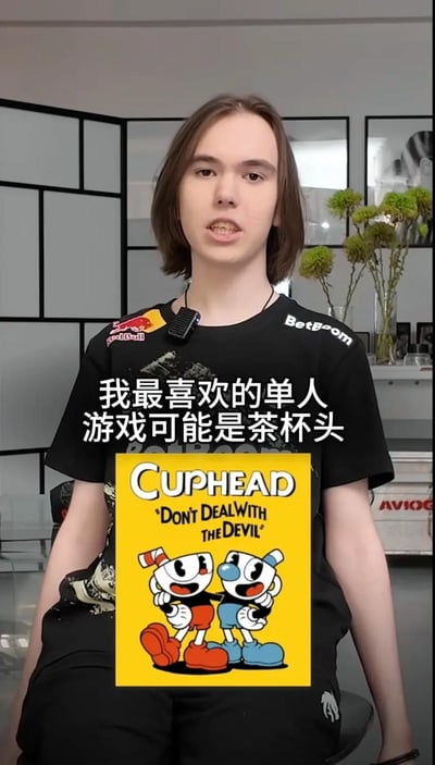 这张图是CS2职业电竞选手donk的采访截图，他穿着带有红牛、BetBoom赞助商标识的黑色战队队服，领口夹着收音麦，处于室内采访场景，背景可见黑色方格隔断、插有绿植的花瓶等陈设。图上叠加了中文配字“我最喜欢的单人游戏可能是茶杯头”，配字下方附带了横版射击游戏《茶杯头（Cuphead）》的黄色封面宣传图，宣传图上印有英文标语“DON'T DEAL WITH THE DEVIL”和两个茶杯头主角卡通形象。