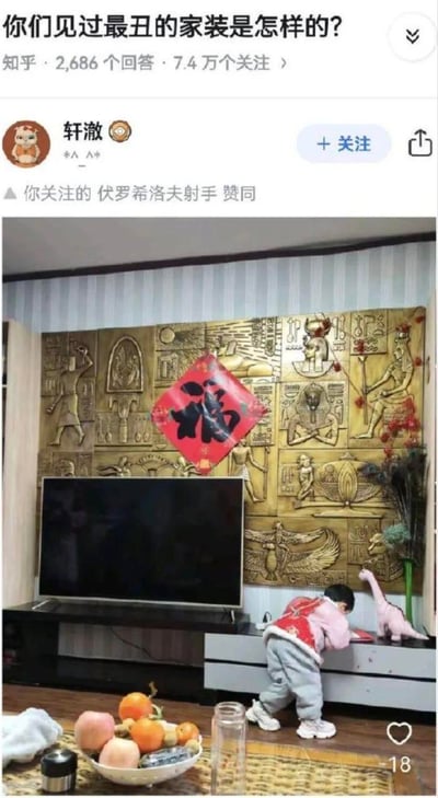 这是知乎家装吐槽问题下的一张真实家庭照片：电视背景墙采用充满古埃及元素的浮雕设计，包含法老、象形文字、埃及神话生物等形象，却在浮雕正中间贴了一个中国传统的红底黑字倒“福”字，两种完全不搭的风格碰撞出强烈的违和感，显得格外搞笑。画面里小孩在电视柜前玩耍，前景摆放着水果盘等家居物品，整体场景充满生活化的迷惑感。
无谐音梗或双关，仅为风格混搭带来的视觉反差效果。