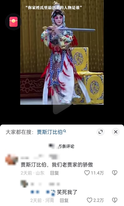 这是一张竖屏的短视频平台界面截图，上半部分是经典京剧《霸王别姬》中虞姬的表演画面，配文提问“你家姓氏里最出名的人物是谁”；下半部分是评论区内容，一位山东网友的评论“贾斯汀比伯，我们老贾家的骄傲”获得了11.4万点赞，另有河南网友回复“笑死我了”，同时页面顶部的搜索栏显示“大家都在搜：贾斯汀比伯”。网友利用贾斯汀·比伯中文译名里的“贾”姓，将这位外国歌手和中文贾姓关联起来，玩起了谐音姓氏梗，制造出反差感十足的搞笑效果，引发了其他网友的互动和相关搜索热度。