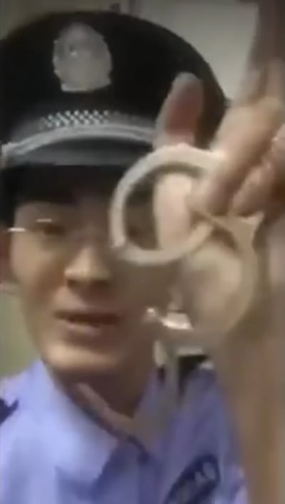 一名身穿蓝色警服、头戴警帽的警察正手持一副手铐展示在镜头前，画面为近距离特写，背景模糊。