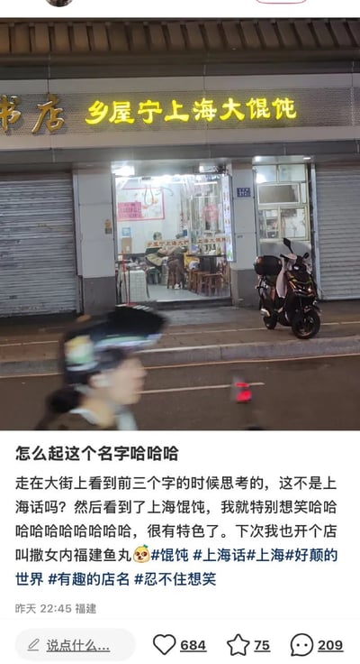 图片展示了一家夜间营业的馄饨店门面，招牌用黄色大字写着'乡屋宁上海大馄饨'。店门口停放着一辆电动车，有行人模糊走过。图片下方是来自福建用户的评论，称看到'乡屋宁'三个字时联想到上海话，觉得与'上海大馄饨'组合十分有趣好笑，并开玩笑说下次要开一家叫'撒女内福建鱼丸'的店，附带#馄饨 #上海话 #有趣的店名 等话题标签。