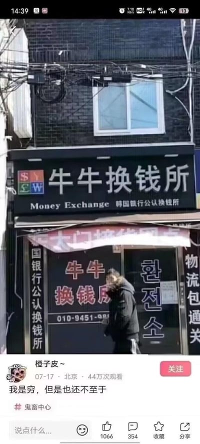 这是一张抖音平台的竖屏社交媒体截图，画面上半部分是街头一家名为“牛牛换钱所”的店铺，该店铺为韩国银行公认换钱所，招牌、门面上印有中韩文对照的“牛牛换钱所”“환전소”字样，还有英文“Money Exchange”以及联系电话“010-9451-98”，店铺两侧竖牌分别标注“国银行公认换钱所”和“物流包通关”，一名穿黑色外套的行人正从店铺门前走过。画面下半部分是抖音用户“橙子皮~”的发布界面，该用户定位北京，于07-17发布此内容，配文“我是穷，但是也还不至于”，内容归类在“鬼畜中心”分区，累计获得44万次观看、1066个赞、354条评论。这个内容的笑点在于“牛牛换钱所”的名称谐音“扭扭捏捏换钱所”，被网友联想为和“穷到扭捏换钱”相关，发布者的配文借这个谐音梗自嘲，表达自己虽穷但还没到需要来此处的程度，充满搞笑和自嘲的氛围。