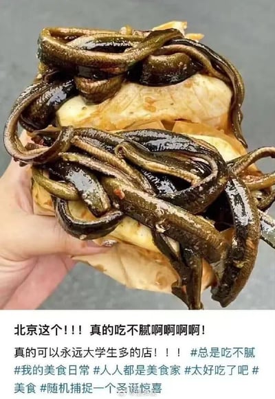 一只手拿着一个堆叠着大量鳝鱼的三明治，鳝鱼呈现深色，看起来油亮有光泽。图片下方有文字评论，表达对这道北京美食的喜爱，称其百吃不腻，特别受大学生欢迎。