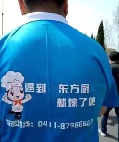 图片展示了一位身穿蓝色厨师服人员的背影，服装左侧印有戴厨师帽的卡通厨师形象，中间有白色文字“遇到 东方厨 就嫁了吧”，底部标注“报名热线：0411-87966600”。背景为户外场景，可见树木与蓝天，推测为厨师职业相关的宣传服装。
