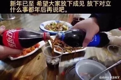 这是一张新年主题的搞笑创意静态梗图，属于图文混排的文字加注图。画面呈现餐桌聚餐场景，桌上摆放着几盘菜肴，两只手分别拿着可口可乐和百事可乐，正同时往同一个玻璃杯中倒饮料。图的上方配有文字“新年已至 希望大家放下成见 放下对立 什么事都年后再说吧。”，创作者用可口可乐与百事可乐这对常被大众拿来对比、存在“品牌对立”趣味话题的饮品，隐喻生活中存在分歧、对立的双方，借新年的氛围传递出暂时放下矛盾、和解的意味，同时也带着“暂时搁置问题，年后再处理”的调侃感，用幽默的方式贴合新年的社交情绪。