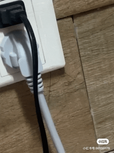 这是一个创意改编自'广式双马尾'梗的动图，通过巧妙的视觉错位，将插座上的插头和电线组合想象成蟑螂的形态。动图展示了一个白色插座上插着一个黑白相间的插头，垂下的电线在轻微晃动中仿佛蟑螂的触角和身体在移动，幽默地呼应了'广式双马尾'中将蟑螂触角比作双马尾的核心创意。