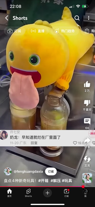 这是YouTube Shorts平台的短视频截图，画面中黄色的奶龙毛绒玩具被放置在饮品制作机上，它的长舌头搭在装有饮品的杯子上，看起来像是被“征用”来辅助制作饮料，场景滑稽。下方的热门评论以奶龙的口吻吐槽“早知道就烂在厂里面了”，精准戳中玩具被用于奇怪用途的笑点，让这个趣味画面更添搞笑氛围。