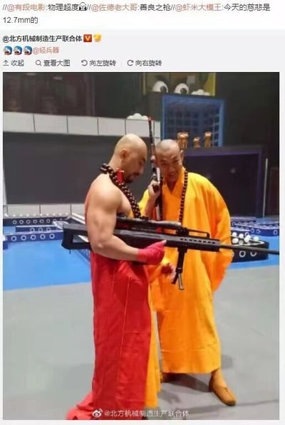 这是一张结合视觉创作与文字玩梗的社交媒体截图，画面主体是两位身着僧袍的真人：一位穿红色僧袍的健壮人物手持一把12.7mm口径的大狙击步枪，姿态沉稳；另一位穿黄色僧袍的人物面带笑容，将一把小型步枪贴在耳边，仿佛在“听枪”。上方的微博转发区域里，网友用“物理超度”“善良之枪”“今天的慈悲是12.7mm的”等文字玩梗，利用“慈悲”与“击毙”的谐音，结合和尚的宗教身份与枪械的攻击性形成强烈反差，制造出荒诞幽默的效果，属于典型的谐音反差类趣味内容。