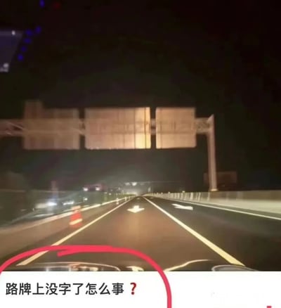 夜间高速公路场景，从车内视角拍摄，前方道路有对向车流灯光，左侧车道旁可见橙色交通锥。道路上方横跨的大型路牌显示为空白状态，无任何文字信息。图片底部有红色圆圈标注并配有文字'路牌上没字了怎么事？'，直观表达了对路牌异常情况的疑惑。