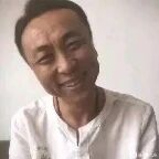 图片中是一位穿着白色上衣的男性，面带自然的微笑，背景为浅色，整体给人亲切、平和的感觉。
