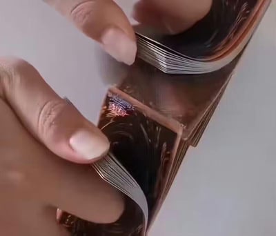 这是一张利用视觉错位原理拍摄的趣味图片：一双手分别捏住一叠卡片的上下部分，通过特定的拍摄角度，让原本平整叠放的卡片看起来像是被硬生生掰出了弧度，制造出违背物理常识的神奇视觉效果，给人新奇有趣的观感。
无双关、谐音梗或暗示类内容。
