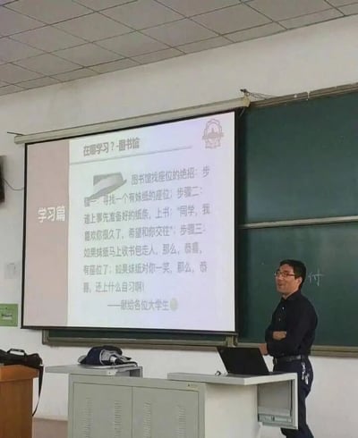 这是一张在大学校园教室拍摄的真实场景照片，画面右侧有一位戴眼镜的男教师，双臂交叉站在讲台旁，脸上带着笑容，神态轻松。讲台上方的投影幕布展示着以“学习篇”为主题的内容，核心是“在哪学习？-图书馆”，其中分享了一个充满调侃意味的图书馆找座位“绝招”：第一步是寻找有女生的座位，第二步是递上写有“同学，我喜欢你很久了，希望和你交往”的纸条，第三步则根据女生的不同反应给出两种趣味结果——如果女生马上收书包走人，就成功获得座位；如果女生对自己一笑，就不用再上自习，末尾还标注“献给各位大学生”。整个内容用幽默的方式结合了图书馆找座的困扰和校园恋爱的趣味，让原本严肃的课堂氛围变得轻松活泼。