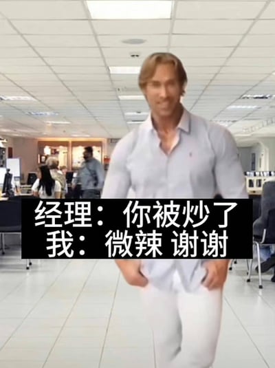 图片中美国健身网红迈克·奥赫恩身着浅色衬衫和白色裤子，双手插兜，带着标志性的迷之自信表情行走在办公室中。背景可见其他办公人员和办公设备。图片下方有黑色背景白色文字的对白：“经理：你被炒了 我：微辣 谢谢”。这是“大力王文学”的典型表现形式，通过无逻辑的对话回应，以幽默方式讽刺盲目自信的态度，是年轻人用于职场吐槽和情绪宣泄的梗图。