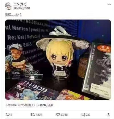 该图片为Twitter用户@Nin2_9510（昵称“二少(Nin)”）发布的帖子截图，内容是一张桌面布置照片。桌面上有一个金发Q版女仆装手办，头戴白色蕾丝帽，表情疑惑微撅嘴，立于透明底座上。手办左侧有一个戴耳机、手持杯子的人物立牌，背景是显示滚动文字的屏幕。桌面上还散落着印有“TH909”字样的杂志和标有“SAMPLE”的物品。帖子配文“躾理……？”（意为“礼仪……？”），可能暗示对桌面布置或手办表情的调侃。