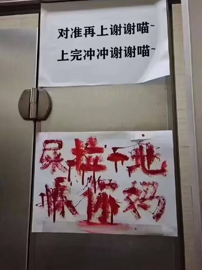 图片展示了一扇金属门上贴着两张提示语纸条。上方纸条用黑色打印体写着“对准再上谢谢喵~ 上完冲冲谢谢喵~”，语气可爱礼貌，带有“喵~”的萌系后缀；下方纸条则用红色类似血渍的颜料手写着“屎拉干地操你妈”，字迹潦草狂放，内容粗俗攻击性强。两张纸条形成鲜明对比，展现了公共场合提示语从礼貌到愤怒的极端情绪转变。