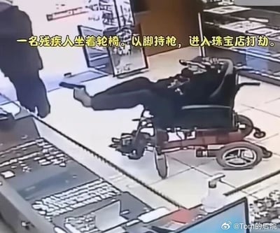 这是一张珠宝店的监控画面截图，画面可见一名下肢残疾的男子乘坐电动轮椅进入店内，他将双腿抬起，用脚握持枪支对准珠宝店的陈列柜台方向，柜台后方站有一名工作人员，画面上方配有黄色醒目文字标注事件内容：“一名残疾人坐着轮椅。以脚持枪，进入珠宝店打劫。”，画面右下角带有微博账号水印，店内的珠宝陈列柜、地面瓷砖等环境元素清晰可见，事件场景反常，具备较高的话题性。