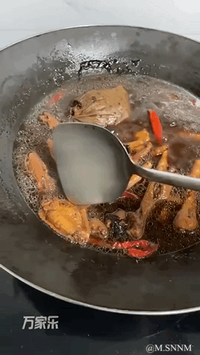 这是一段动态GIF，展示了在黑色铁锅中炖煮卤味食材的场景。锅里的汤汁翻滚冒泡，可见炖煮的肉块、红辣椒和卤料包，金属锅铲正在翻动食材，整个画面充满烹饪的烟火气，呈现出卤味菜肴的制作过程。