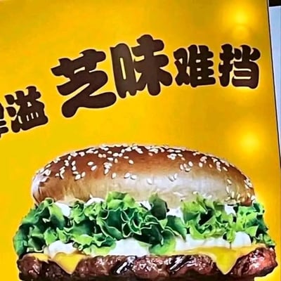 这是一张芝士汉堡的商业宣传海报，背景采用亮眼的暖黄色调，视觉吸引力强。海报下半部分展示了一款用料丰富的芝士汉堡：表面撒满白芝麻的松软面包胚，铺着新鲜翠绿的生菜，搭配绵密的白色酱料，下方是厚实多汁的肉饼，肉饼上覆盖着融化后微微流淌的芝士，整体外观诱人，充满食欲。海报上方配有文字“溢 芝味难挡”，运用了谐音梗，将“滋味难挡”的“滋”替换为“芝士”的“芝”，既巧妙点明了产品含有芝士的核心特点，又突出了汉堡风味绝佳、让人难以抗拒的卖点。