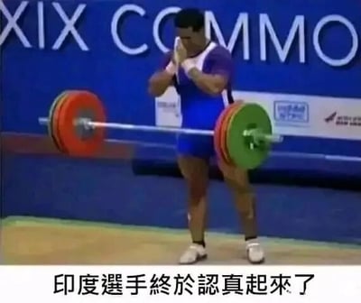 这是一张利用视觉错位制造笑点的搞笑梗图，画面中是一位身处举重赛事场地的男性举重运动员，他双手合十置于脸前，做出类似祈祷或准备发力的动作，而杠铃的位置恰好与他的双腿重叠，形成了杠铃卡在他腿间、他并未真正握住杠铃的错觉。图片下方配有文字“印度选手终于认真起来了”，结合视觉错位的效果，调侃这位选手看似认真准备，实则呈现出滑稽的画面，通过这种反差感制造幽默效果。