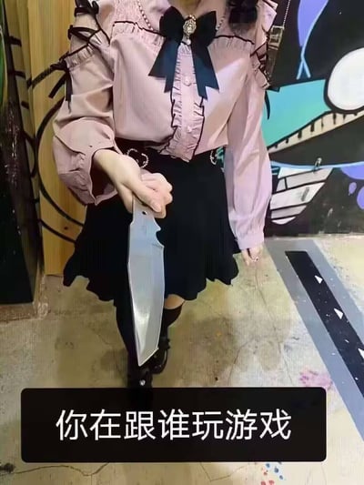 图片中显示一位穿着粉色蕾丝衬衫和黑色短裙的年轻女性，她右手手持一把银色的大型刀具，刀刃锋利。背景是一面有彩色涂鸦的墙壁，地面看起来是水泥材质。图片底部有一行黑色背景白色文字："你在跟谁玩游戏"。人物表情不清晰，但整体姿态给人一种紧张或威胁的感觉。