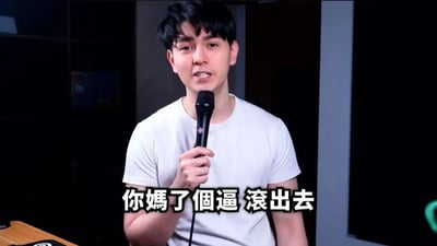 本图是一位身穿白色T恤、手持麦克风的年轻男子，下方配有大字粗体字幕“你媽了個逼 滾出去”。整体氛围非常直白、情绪激烈，表达了极强的不满、怒骂和驱赶的情绪。这句话为网络常见爆粗用语，通常用于调侃、激烈冲突或玩笑性质的发泄，属于情绪发泄型梗图。

本图片并未涉及双关、谐音，但有网络流行粗口色彩，适合用于怼人、斗图、宣泄情绪场景。