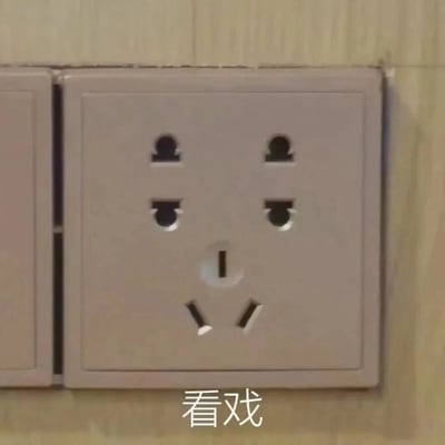 一张拍摄日常家用插座的照片，插座上的孔洞排列恰好形成了类似人脸的表情：上方两个圆孔像眼睛，中间两个圆孔像鼻孔，下方的三孔插座像嘴巴。图片下方配有白色文字“看戏”，将插座拟人化，仿佛它正带着吃瓜看戏的表情注视着前方。这种将日常物品通过创意联想转化为趣味表情包的形式，展现了网友的幽默感和观察力。