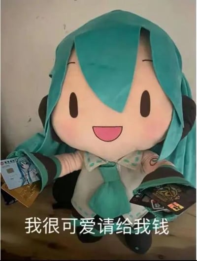 这张图展示了一个大尺寸的初音未来毛绒玩偶，玩偶有着标志性的蓝绿色长发，脸上露出开心大笑的表情，双手分别拿着几张银行卡或会员卡类的卡片，图片下方配有醒目的文字“我很可爱请给我钱”。图中没有双关、谐音梗或暗示内容，而是利用可爱的虚拟偶像毛绒形象搭配直白的求钱文字，形成反差萌的搞笑效果，通常用来以撒娇、俏皮的方式向他人索要零花钱、活动经费等，适合在朋友之间或者ACG社群中用来玩梗。