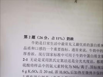 这是一张翻拍的专业化学/食品检测类试题页面，内容聚焦于牛奶中蛋白质含量的测定方法。页面显示为试卷第2题（分值26分，占比11%），主题为“奶浓”，先介绍了牛奶作为优质蛋白质来源，蛋白质是衡量其品质的重要指标，随后2-1小节引入凯氏定氮法、分光光度法测定蛋白质的前置操作——将样品氮元素转化为NH₄⁺离子，还提及国标规定的试剂用量（6g K₂SO₄及20mL浓H₂SO₄）与加热操作，但题目后半部分被截断未显示完整。