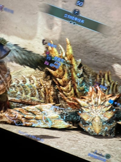 这是一张《怪物猎人》系列游戏的屏幕截图，场景设定在沙漠地图中，画面主体是被玩家击败的爆锤龙尸体，其布满尖刺和粗糙甲壳的躯体清晰可见；画面左侧露出猎人角色的部分身形，屏幕上方显示带有“立刻结束任务”字样的任务UI栏，还有数字“50”的标识，爆锤龙尸体上方标注有“爆锤龙 尸体”的提示文字，右下角则显示道具“投射器闪光弹”的剩余数量为2/3。整体呈现出玩家成功完成狩猎任务后的场景，此时玩家可选择结束任务返回据点，或对怪物尸体进行素材剥取。