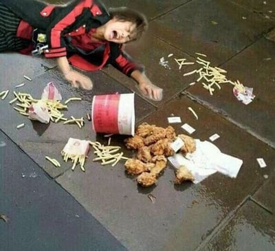 这是一张经过P图改编的照片，画面里一个穿着红黑相间外套的人趴在湿漉漉的地面上，大张着嘴，表情看起来十分痛苦崩溃，双手向前伸，似乎想要挽回什么。在他身前，是打翻的肯德基全家桶包装，炸鸡腿、薯条散落一地，食物沾到了地面上，看起来已经无法食用。这张图通过夸张的表情和场景，放大了人们面对喜爱的美食被打翻时的心疼情绪，制造出搞笑的效果，让有过类似经历的人产生共鸣。