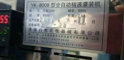 这是一张原始拍摄的设备铭牌照片，主体是一块金属材质的设备参数铭牌，安装在YK-8008型全自动精液灌装机上。铭牌上清晰标注了该设备的核心电气参数：电压为交流220V、频率50Hz、功率400W、电流2.5A；同时记录了设备的生产日期为2021年8月11日，设备编号为21-28。铭牌下方标注了生产企业为济南约克农牧器械有限公司，附带了公司地址、技术支持电话和官方网址。图片左侧还露出了设备的一部分显示屏，上面显示数字“55”和“5”，进一步表明这是设备实拍场景。该设备属于畜牧养殖领域的专用器械，用于精液的自动化灌装工作。