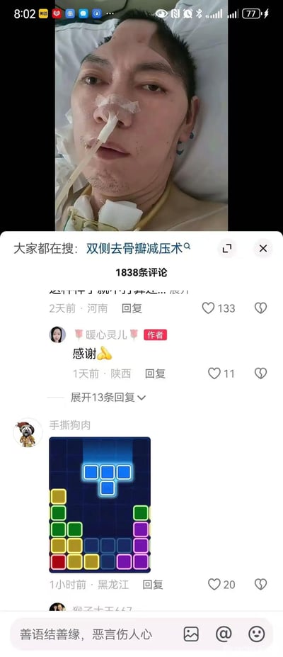 这是一张抖音平台的社交媒体评论区截图，上方展示了一位刚完成双侧去骨瓣减压术的患者，他躺在床上，头部呈现术后的特征，鼻饲管插在鼻腔，颈部有包扎，神情平静虚弱；下方评论区中，账号「暖心灵儿」（内容作者）回复网友表达感谢，另有账号「手撕狗肉」发布了一张方块消除游戏的截图，玩了视觉相似的梗——患者术后的头部形状与游戏里的蓝色方块组形状高度相似，以此在评论区玩梗，属于网络社区里的趣味互动，同时也带有一丝心酸感。