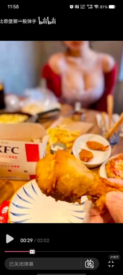 这是一张美食视频的截图，画面中央是一只金黄诱人的炸鸡腿被拿在手中，特写镜头突出了鸡腿的酥脆质感。背景中可以看到一张摆满食物的餐桌，包括KFC的外卖盒、薯条、炸鸡块和部分披萨。视频播放器显示当前播放时间为00:29，总时长2:02，弹幕功能已关闭。