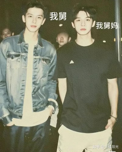 这是一张粉丝二创的趣味梗图，图中左侧为演员张晚意，右侧为演员邓为，二人因合作古装剧《长相思》，其饰演的玱玹与涂山璟被网友组成CP，于是被粉丝在同框照片上标注“我舅”“我舅妈”的文字，玩起性别反转的搞笑梗。照片呈现复古胶片质感，两人站姿放松，表情平静，背景还有模糊的路人身影。