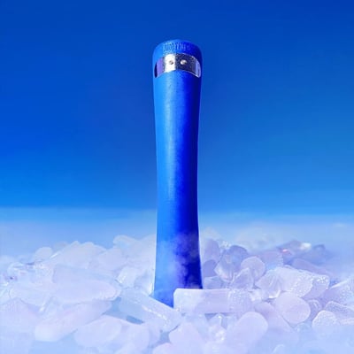 图片主体为一个蓝色圆柱形设备，顶部带有银色装饰环，表面印有“SMOK”品牌标识。设备直立放置在散落的透明冰块上，底部有轻微的雾气效果，背景是渐变的纯净蓝色，整体营造出冷冽、清新的视觉氛围。画面简洁，无其他多余元素，突出产品本身的设计与质感。