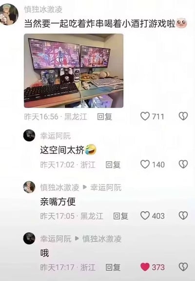 社交媒体截图展示了一个情侣电竞桌场景，桌上有两台显示器显示游戏画面，旁边摆放着炸串、饮料和零食。评论区互动幽默，用户"幸运阿阮"说"这空间太挤😂"，而原作者"慎独冰激凌"回复"亲嘴方便"，引发有趣对话。