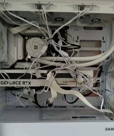 这是一张白色主题台式电脑内部的实拍照片，可见微星主板、带有"GEFORCE RTX"和"ULTRA"标识的白色系显卡，以及白色CPU散热器，硬件配置偏向中高端，但内部的各类供电线、数据线完全未做整理，相互缠绕在一起，杂乱无章，彻底破坏了白色主机的整洁美观性，不仅可能影响机箱内部散热，也成为了装机理线的典型反面案例，极具吐槽点。