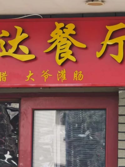 图片展示了一家餐厅的红色招牌，上方用黄色大字写着“达餐厅”，下方小字为“腊大爷灌肠”。招牌下方是红色的门，门上有玻璃窗，整体看起来是街边常见的餐馆门面。