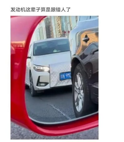 图片展示了一辆红色汽车的侧后视镜视角，镜中反射出一辆白色轿车正处于狭窄空间中，似乎被夹在另一辆车和拍摄车之间，可能是在停车或行驶时遇到的尴尬路况。图片顶部配有文字“发动机这辈子算是跟错人了”，通过拟人化的手法，幽默地调侃驾驶员技术不佳，让汽车发动机“受了委屈”，营造出搞笑又无奈的氛围。
