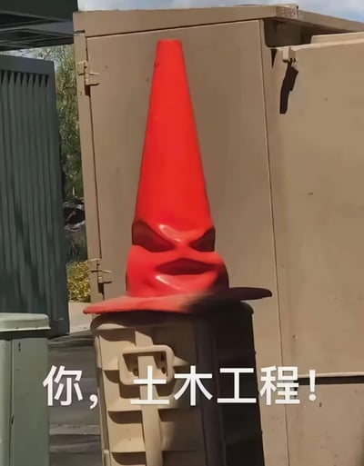 这是一张利用视觉错位形成的趣味照片，红色路锥的底部与下方箱体的把手、阴影组合，恰好构成了一个带着愤怒严肃表情的“人脸”，仿佛正在严肃喊话。图下方配有文字“你，土木工程！”，用这种戏谑的方式调侃土木工程专业，营造出一种被“点名”的搞笑反差感。
视觉错位说明：路锥下部的阴影形成类似眼睛的形状，箱体的把手则构成了嘴部，从而形成人脸的错觉。