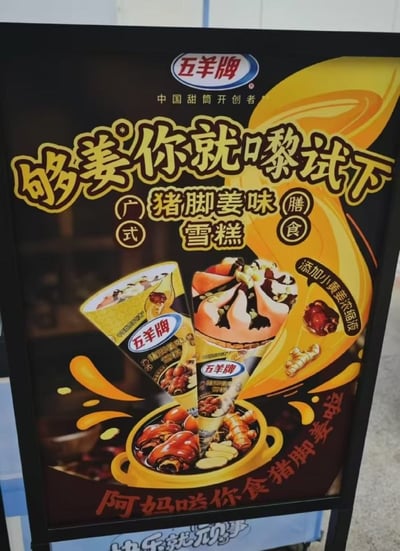 这是一张冷饮品牌五羊牌的新品线下宣传海报，整体以深色调为底色，顶部印有五羊牌品牌标识及“中国甜筒开创者”的品牌标注。主宣传语采用粤语谐音双关设计“够姜你就嚟试下”，其中“够姜”既指代产品添加姜类原料的属性，也是粤语中“有种你就来”的通俗表达，契合广东地域文化特色。海报标明该新品为广式膳食类猪脚姜味雪糕，添加小黄姜浓缩液，画面中部展示了该款甜筒雪糕的实物样式，下方搭配盛有猪脚、姜块、鸡蛋等传统猪脚姜食材的砂锅图案，底部配有极具广式生活感的话术“阿妈叫你食猪脚姜啦”，整体设计风格活泼，突出了新品的地域特色和猎奇口味属性。