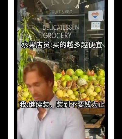 这是一张趣味梗图，背景是一家标注有英文“FRUIT & VEG”“DELICATESSEN GROCERY”的水果店，店面前方摆放着一堆品类丰富的水果；前景是一位穿着浅色衬衫的男性，他表情无奈、低头前倾，似乎对某种情况感到无语。图中配有两组中文对话文字：水果店员说道“买的越多越便宜”，顾客则回应“继续装，装到不要钱为止”，通过夸张地延伸商家“买多优惠”的促销逻辑，用极端的“装到免费”的回应制造出反差笑点，是对日常消费促销场景的幽默调侃。