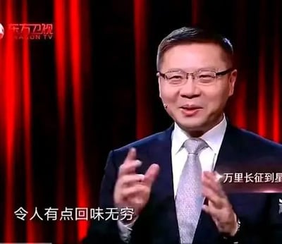 图片中是一位身着深色西装、白色衬衫并系着银色领带的男子，正在红色幕布背景的舞台上发言。他双手做出手势，面带微笑，神情专注。左上角有'东方卫视'（Dragon TV）的水印标识。图片底部有字幕文字'令人有点回味无穷'，右侧还有部分文字'万里长征到星'（可能为节目中的台词片段）。整体场景看起来是电视节目中的演讲或访谈环节。