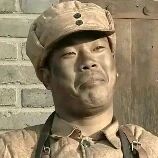 图片中展示了一位身穿军装的男性人物，他戴着带有纽扣的军帽，身着旧式军装，肩部有肩带，背景是灰色的砖墙。人物面部表情平静，目视前方，整体画面呈现出一种历史场景的氛围。