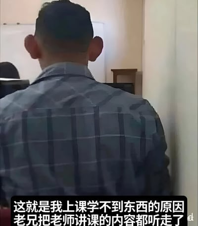图片展示了一位身穿蓝灰色格子衬衫的男性背影，他留着短发，正坐在教室中面向前方。图片底部配有文字：“这就是我上课学不到东西的原因 老兄把老师讲课的内容都听走了”，以幽默调侃的方式将自己上课学不到知识的原因归咎于前排同学“听走了”老师讲的内容，展现了学生群体中常见的自嘲式搞笑场景。
