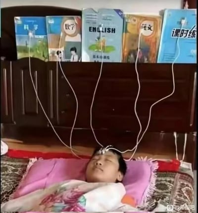 这是一张经过P图改编的搞笑照片，图中一名学生躺在床上，双眼紧闭，额头处连接着几根白色的线，线的另一端分别连接在《科学》《数学》《ENGLISH（英语）》《语文》《课时练》这几本常见的中小学课本上，模仿输液或者电子设备充电的形式，仿佛要通过这种方式直接把课本里的知识“输入”进大脑。这张图用夸张且具象的创意，调侃了学生面对繁重的课业压力，渴望快速吸收知识、减轻学习负担的无奈又搞笑的心态，精准戳中了学生群体的学习焦虑，引发共鸣。